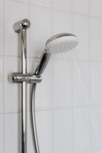 Close-up of a chrome shower head with water flowing, showcasing sleek modern bathroom design.